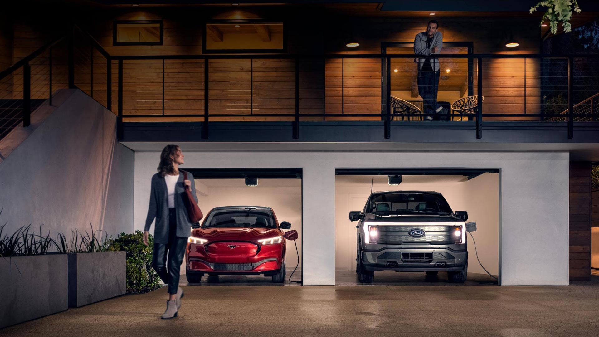 Woman walking out from home garage with a 2024 Mustang® Mach-E and Ford Lightning® truck in plugged-in and charging | Bozard Ford in Saint Augustine FL